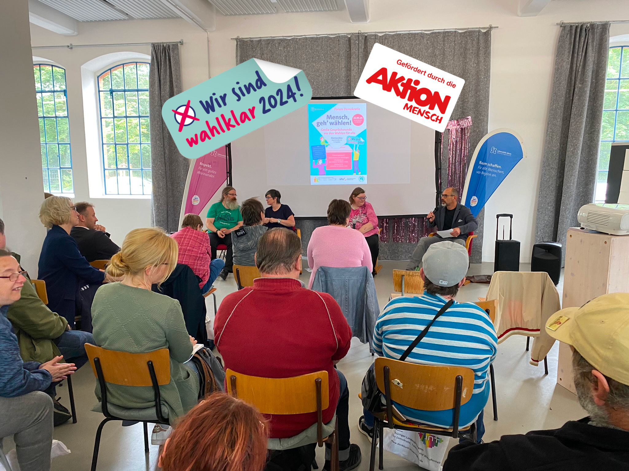 Auf einem Podium sitzen 4 Personen und sprechen über Wahlen. Das Publikum ist von hinten zu sehen.