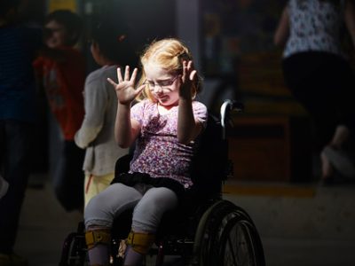 Mädchen im Rollstuhl hebt die Arme